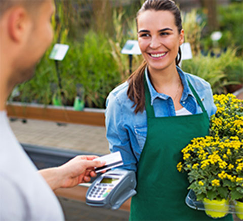 Man using credit card to purchase potted flowers from woman